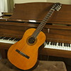 Photo of a Guild nylon string guitar leaning against the keyboard of a grand piano.